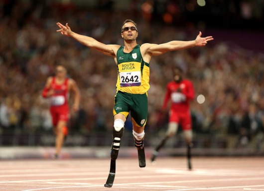 Định mệnh đã lấy đi của Oscar Pistorius đôi chân, khiến anh phải sống đời tàn tật từ khi cất tiếng khóc lọt lòng. Nhưng từ sâu thẳm trái tim mình, “người không chân” chưa bao giờ có ý nghĩ đầu hàng số phận. Hơn mười năm miệt mài băng mình trên đường chạy, nâng cơ thể mình bằng đôi chân sợi các-bon, Pistorius muốn chứng minh cho cả thế giới thấy rằng những người không may bị khuyết một phần cơ thể như anh vẫn có quyền mơ đến mọi đỉnh cao. Olympic 2012, Pistorius cuối cùng đã thỏa nguyện. Oscar Pistorius – “Người không chân” chinh phục cả thế giới Qua cơn đau bằng máu và nước mắt Pistorius đã trở nên nổi tiếng khắp thế giới, kể từ khi anh bước ra đấu trường Paralympic 2004 và giành mọi HCV ở những cự ly chạy quan trọng nhất. Tại Athens năm đó, hàng vạn khán giả đã tung hô anh như một thần tượng lớn với danh hiệu người không chân chạy nhanh nhất hành tinh. Nhưng ở Nam Phi, thay vì cái danh hiệu dài lê thê đó, người ta vẫn trìu mến gọi anh bằng cái tên Oscar. Một đồng đội bình thường (hoàn toàn lành lặn) ở đội tuyển điền kinh Nam Phi dự Olympic 2012 đã lý giải: “Chỉ với cách gọi ấy, chúng tôi mới thể hiện được hết lòng kính phục của mình. Oscar không chỉ là một VĐV thể thao xuất sắc. Nỗi bất hạnh cuộc đời mà anh ấy phải chịu đựng và vượt qua xứng đáng là một biểu tượng về ý chí vươn lên cho hàng tỷ người trên khắp hành tinh này”. Người đồng đội của Pistorius không hề quá lời. Tại đất nước từng sản sinh ra huyền thoại Nelson Mandela, từng giành quyền đăng cai vòng chung kết World Cup 2010, Oscar Pistorius vẫn thường được mang ra làm tấm gương cho lũ trẻ. Khi các nhà báo nước ngoài lặn lội về tận Nam Phi trước Thế vận hội 2012, họ đã được nghe kể về quá khứ đầy nước mắt của Oscar. 11 tháng tuổi, anh đã bị bác sỹ kết luận căn bệnh không có xương mác bẩm sinh là vô phương chữa trị. Vì căn bệnh ấy, Oscar không thể có chân và suốt cuộc đời phải gắn bó cùng đôi chân giả hoặc chiếc xe lăn. Tuổi ấu thơ trải qua nhiều ký ức về một nỗi ám ảnh kinh khủng. Pistorius từng kể rằng anh đã khóc hàng trăm lần khi nhìn những đứa trẻ cùng trang lứa với mình đá bóng, chạy chơi trên đường hoặc làm bất cứ điều gì đó với đôi chân lành lặn, nhưng nỗi đau lớn ấy không thể đánh gục ý chí của Pistorius. Thay vì tự thu mình vào bóng tối, Pistorius xin cha mẹ đưa đến bệnh viện để tìm kiếm cơ hội khôi phục” đôi chân. Chuyện tái tạo xương mác dĩ nhiên là vô vọng, song các bác sỹ đã giúp Pistorius một đôi chân sợi các-bon rất bền và vừa vặn để anh tập chạy hàng ngày. Tâm sự cùng báo giới bên lề Olympic, “người không chân” bảo rằng suốt hơn mười năm qua, anh đã chạy nhiều đến mức điểm tiếp xúc giữa cơ đùi với đôi chân sợi các bon tứa máu đầy đau đớn. Có những lúc, sự mệt mỏi quá độ về thể xác thậm chí khiến anh phải ngã gục ngay trên đường chạy của mình, nhưng Oscar Pistorius đã vượt qua tất cả bằng thần kinh thép và nghị lực phi thường. Câu chuyện về một huyền thoại Olympic bắt đầu, chính từ những tháng ngày cay cực như thế. “Bay” trên đỉnh cao Lẽ ra, Oscar Pistorius đã có thể tham dự Olympic từ năm 2008. Thời điểm đó, một nghiên cứu của Trường đại học Cologne (Đức) nói rằng Pistorius sẽ tiêu tốn ít hơn các vận động viên bình thường khác 25% năng lượng nhờ đôi chân sợi các-bon nên không thể để anh thi đấu tại vòng loại Olympic. Vì chuyện này, Oscar Pistorius đã quyết định khiếu nại. Dù Liên đoàn điền kinh thế giới sau đó đã xử thắng cho Pistorius, nhưng việc mất quá nhiều thời gian vào vụ lùm xùm này đã khiến anh không đạt được thành tích đủ tốt để giành vé chính thức đến Bắc Kinh. 4 năm sau, câu chuyện đã hoàn toàn khác. Việc Liên đoàn điền kinh thế giới chính thức cho phép Pistorius thi đấu tại giải Vô địch thế giới tổ chức năm 2011, giống như một sự thừa nhận mặc nhiên rằng Oscar Pistorius phải được đối xử như bất kỳ vận động viên bình thường nào. Phấn khích, Oscar Pistorius đã vượt qua thành tích chuẩn A để đường hoàng giành vé dự Thế vận hội London 2012. Từ đây, một chương mới của thể thao thế giới đã mở ra khi Oscar trở thành vận động viên khuyết tật đầu tiên trong lịch sử dự một kỳ Olympic. Cả đất nước Nam Phi ăn mừng sự kiện đó một cách tự hào. Oscar đã trở thành biểu tượng cho nghị lực, lòng quả cả của cả một dân tộc và Tổng thống Mbeki, thậm chí đã đề nghị Oscar Pistorius nên cầm cờ cho Đoàn thể thao Nam Phi trong lễ khai mạc. Thời khắc lịch sử đã đến hôm 4/8. Oscar Pistorius xuất hiện trên sân Olympics trong sự hò reo của 8 vạn người. Anh khởi động, bước lên bục xuất phát và bứt lên kết thúc vòng loại với vị trí thứ 2 chung cuộc. “Người không chân” đã “chạy” vào đến vòng bán kết cự ly chạy 400m bên cạnh những kỷ lục gia lành lặn. Dù không thể giành được một tấm huy chương sau đó, Pistorius đã khoác lên mình lá cờ Nam Phi. Anh ăn mừng tấm huy chương của riêng mình, tấm huy chương có ý nghĩa không kém gì những kỷ lục thế giới hay Olympic đã được thiết lập bởi những siêu sao lừng danh khác. Từ hôm nay, cả thế giới sẽ phải nghiêng mình chào đón một huyền thoại: Oscar Pistorius Siêu nhân tại Paralympic 2012? Cũng giống như Usain Bolt, Oscar Pistorius đã thống trị toàn bộ những cự ly chạy quan trọng nhất tại Paralympic 4 năm về trước. Trên đất Bắc Kinh, Oscar đã giành 3 HCV trên đường chạy 100m nam, 200m nam và 400m nam. London 2012, ở tuổi 25 sung sức nhất và sau màn trình diễn cực kỳ ấn tượng tại Olympic, Oscar Pistorius được dự báo sẽ bảo vệ dễ dàng những đỉnh cao vinh quang của mình. Một quan chức của Liên đoàn điền kinh thế giới đã ví von: “Nếu coi Usain Bolt là một siêu nhân tại Thế vận hội, thì Oscar chính là siêu nhân ở đấu trường Paralympic”