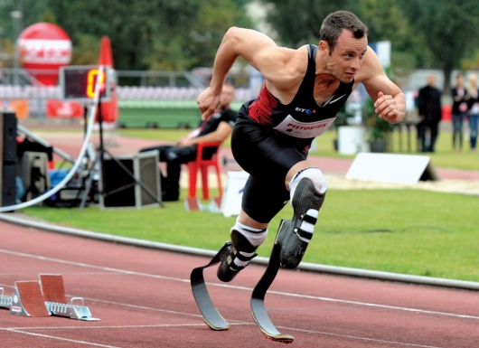 Định mệnh đã lấy đi của Oscar Pistorius đôi chân, khiến anh phải sống đời tàn tật từ khi cất tiếng khóc lọt lòng. Nhưng từ sâu thẳm trái tim mình, “người không chân” chưa bao giờ có ý nghĩ đầu hàng số phận. Hơn mười năm miệt mài băng mình trên đường chạy, nâng cơ thể mình bằng đôi chân sợi các-bon, Pistorius muốn chứng minh cho cả thế giới thấy rằng những người không may bị khuyết một phần cơ thể như anh vẫn có quyền mơ đến mọi đỉnh cao. Olympic 2012, Pistorius cuối cùng đã thỏa nguyện. Oscar Pistorius – “Người không chân” chinh phục cả thế giới Qua cơn đau bằng máu và nước mắt Pistorius đã trở nên nổi tiếng khắp thế giới, kể từ khi anh bước ra đấu trường Paralympic 2004 và giành mọi HCV ở những cự ly chạy quan trọng nhất. Tại Athens năm đó, hàng vạn khán giả đã tung hô anh như một thần tượng lớn với danh hiệu người không chân chạy nhanh nhất hành tinh. Nhưng ở Nam Phi, thay vì cái danh hiệu dài lê thê đó, người ta vẫn trìu mến gọi anh bằng cái tên Oscar. Một đồng đội bình thường (hoàn toàn lành lặn) ở đội tuyển điền kinh Nam Phi dự Olympic 2012 đã lý giải: “Chỉ với cách gọi ấy, chúng tôi mới thể hiện được hết lòng kính phục của mình. Oscar không chỉ là một VĐV thể thao xuất sắc. Nỗi bất hạnh cuộc đời mà anh ấy phải chịu đựng và vượt qua xứng đáng là một biểu tượng về ý chí vươn lên cho hàng tỷ người trên khắp hành tinh này”. Người đồng đội của Pistorius không hề quá lời. Tại đất nước từng sản sinh ra huyền thoại Nelson Mandela, từng giành quyền đăng cai vòng chung kết World Cup 2010, Oscar Pistorius vẫn thường được mang ra làm tấm gương cho lũ trẻ. Khi các nhà báo nước ngoài lặn lội về tận Nam Phi trước Thế vận hội 2012, họ đã được nghe kể về quá khứ đầy nước mắt của Oscar. 11 tháng tuổi, anh đã bị bác sỹ kết luận căn bệnh không có xương mác bẩm sinh là vô phương chữa trị. Vì căn bệnh ấy, Oscar không thể có chân và suốt cuộc đời phải gắn bó cùng đôi chân giả hoặc chiếc xe lăn. Tuổi ấu thơ trải qua nhiều ký ức về một nỗi ám ảnh kinh khủng. Pistorius từng kể rằng anh đã khóc hàng trăm lần khi nhìn những đứa trẻ cùng trang lứa với mình đá bóng, chạy chơi trên đường hoặc làm bất cứ điều gì đó với đôi chân lành lặn, nhưng nỗi đau lớn ấy không thể đánh gục ý chí của Pistorius. Thay vì tự thu mình vào bóng tối, Pistorius xin cha mẹ đưa đến bệnh viện để tìm kiếm cơ hội khôi phục” đôi chân. Chuyện tái tạo xương mác dĩ nhiên là vô vọng, song các bác sỹ đã giúp Pistorius một đôi chân sợi các-bon rất bền và vừa vặn để anh tập chạy hàng ngày. Tâm sự cùng báo giới bên lề Olympic, “người không chân” bảo rằng suốt hơn mười năm qua, anh đã chạy nhiều đến mức điểm tiếp xúc giữa cơ đùi với đôi chân sợi các bon tứa máu đầy đau đớn. Có những lúc, sự mệt mỏi quá độ về thể xác thậm chí khiến anh phải ngã gục ngay trên đường chạy của mình, nhưng Oscar Pistorius đã vượt qua tất cả bằng thần kinh thép và nghị lực phi thường. Câu chuyện về một huyền thoại Olympic bắt đầu, chính từ những tháng ngày cay cực như thế. “Bay” trên đỉnh cao Lẽ ra, Oscar Pistorius đã có thể tham dự Olympic từ năm 2008. Thời điểm đó, một nghiên cứu của Trường đại học Cologne (Đức) nói rằng Pistorius sẽ tiêu tốn ít hơn các vận động viên bình thường khác 25% năng lượng nhờ đôi chân sợi các-bon nên không thể để anh thi đấu tại vòng loại Olympic. Vì chuyện này, Oscar Pistorius đã quyết định khiếu nại. Dù Liên đoàn điền kinh thế giới sau đó đã xử thắng cho Pistorius, nhưng việc mất quá nhiều thời gian vào vụ lùm xùm này đã khiến anh không đạt được thành tích đủ tốt để giành vé chính thức đến Bắc Kinh. 4 năm sau, câu chuyện đã hoàn toàn khác. Việc Liên đoàn điền kinh thế giới chính thức cho phép Pistorius thi đấu tại giải Vô địch thế giới tổ chức năm 2011, giống như một sự thừa nhận mặc nhiên rằng Oscar Pistorius phải được đối xử như bất kỳ vận động viên bình thường nào. Phấn khích, Oscar Pistorius đã vượt qua thành tích chuẩn A để đường hoàng giành vé dự Thế vận hội London 2012. Từ đây, một chương mới của thể thao thế giới đã mở ra khi Oscar trở thành vận động viên khuyết tật đầu tiên trong lịch sử dự một kỳ Olympic. Cả đất nước Nam Phi ăn mừng sự kiện đó một cách tự hào. Oscar đã trở thành biểu tượng cho nghị lực, lòng quả cả của cả một dân tộc và Tổng thống Mbeki, thậm chí đã đề nghị Oscar Pistorius nên cầm cờ cho Đoàn thể thao Nam Phi trong lễ khai mạc. Thời khắc lịch sử đã đến hôm 4/8. Oscar Pistorius xuất hiện trên sân Olympics trong sự hò reo của 8 vạn người. Anh khởi động, bước lên bục xuất phát và bứt lên kết thúc vòng loại với vị trí thứ 2 chung cuộc. “Người không chân” đã “chạy” vào đến vòng bán kết cự ly chạy 400m bên cạnh những kỷ lục gia lành lặn. Dù không thể giành được một tấm huy chương sau đó, Pistorius đã khoác lên mình lá cờ Nam Phi. Anh ăn mừng tấm huy chương của riêng mình, tấm huy chương có ý nghĩa không kém gì những kỷ lục thế giới hay Olympic đã được thiết lập bởi những siêu sao lừng danh khác. Từ hôm nay, cả thế giới sẽ phải nghiêng mình chào đón một huyền thoại: Oscar Pistorius Siêu nhân tại Paralympic 2012? Cũng giống như Usain Bolt, Oscar Pistorius đã thống trị toàn bộ những cự ly chạy quan trọng nhất tại Paralympic 4 năm về trước. Trên đất Bắc Kinh, Oscar đã giành 3 HCV trên đường chạy 100m nam, 200m nam và 400m nam. London 2012, ở tuổi 25 sung sức nhất và sau màn trình diễn cực kỳ ấn tượng tại Olympic, Oscar Pistorius được dự báo sẽ bảo vệ dễ dàng những đỉnh cao vinh quang của mình. Một quan chức của Liên đoàn điền kinh thế giới đã ví von: “Nếu coi Usain Bolt là một siêu nhân tại Thế vận hội, thì Oscar chính là siêu nhân ở đấu trường Paralympic”